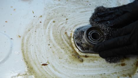 using two hands wearing black gloves to remove the dirt around the in burned gas stove