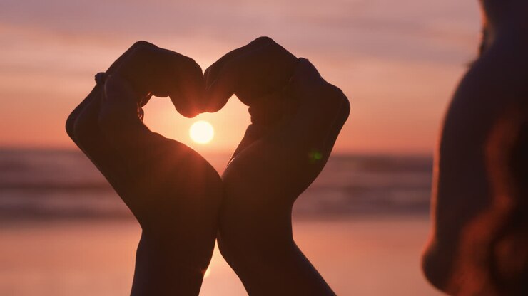 clsoe up mani di donna che fanno la forma di un cuore gesto che tiene un bel tramonto fiamma godendo di vacanze romantiche sulla spiaggia