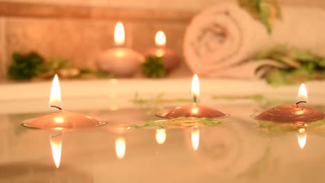 relajante fondo de spa con velas flotando en el agua del baño, algunos pétalos verdes y una toalla cerca de la superficie del agua