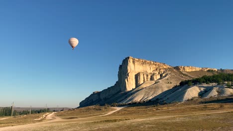 a large white balloon with a basket for flying people flies against a clear blue sky without clouds and against the backdrop of a high beautiful white rock