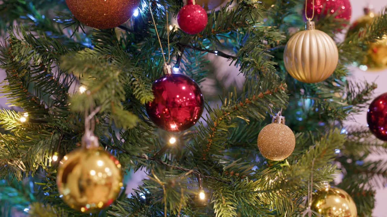 Festive close-up of a Christmas tree adorned with red and gold ornaments, glowing lights, and sparkling decorations.