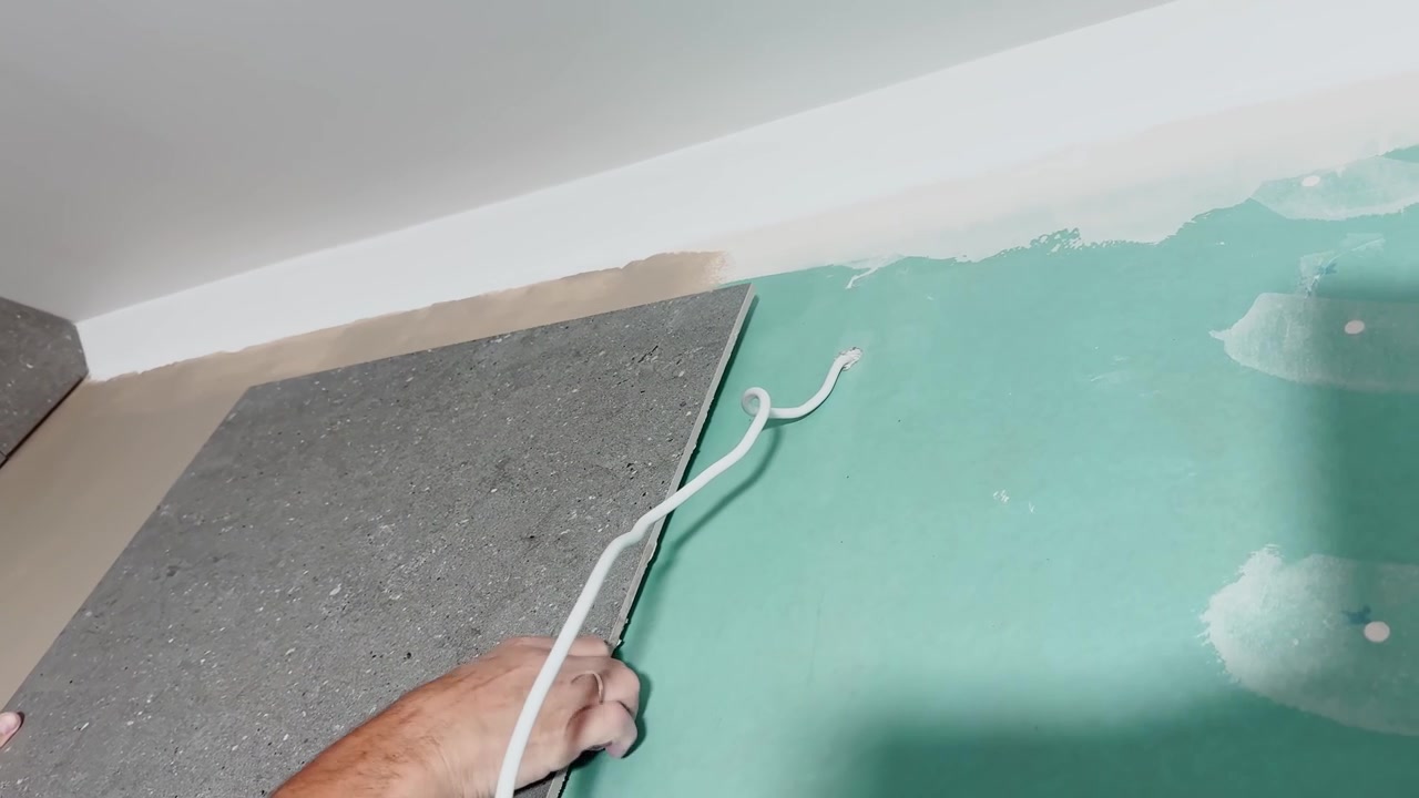 Close-up of a worker positioning a large gray wall tile over a prepared backing surface during an indoor renovation, showing careful alignment and professional installation.