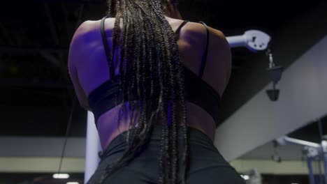 fit girl in the gym using a cable machine while the camera orbits from left to right behind her back