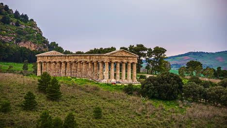 blick auf touristen, die den dorischen tempel von segesta, provinz trapani, sizilien, italien, tagsüber im zeitraffer besuchen, umgeben von hügeligem gelände