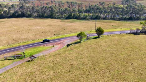 a single car travels on a winding country road through open grassy fields, captured in daylight with smooth aerial camera movement and natural lighting