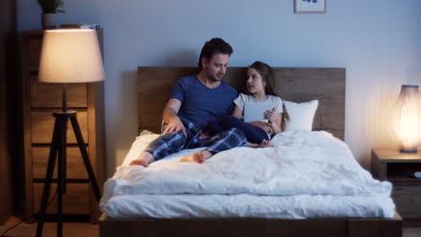 padre caucásico acostado en la cama con su linda hijita desplazándose y grabando en la tableta por la noche