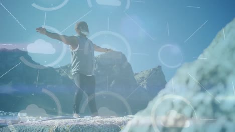 animation of media icons over senior african american man practicing yoga at beach