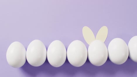 white easter eggs with rabbit ears on purple background with copy space