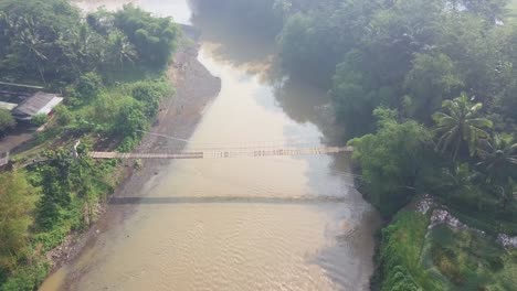 poi drone shot of suspension bridge over the river with motorcycle crossing on it in the morning with sun ray, central java, indonesia