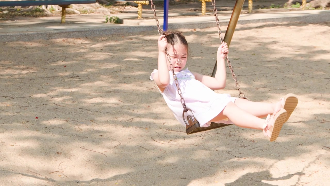 Una niña asiática joven se columpia en un columpio de parque infantil en el Parque Lumpini, Bangkok.