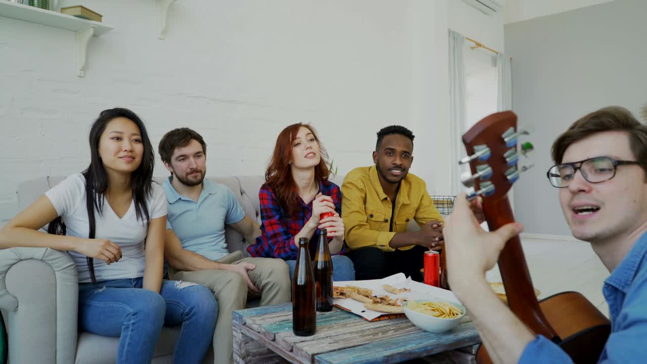 Giovani amici felici fanno festa suonando la chitarra e cantando insieme a casa