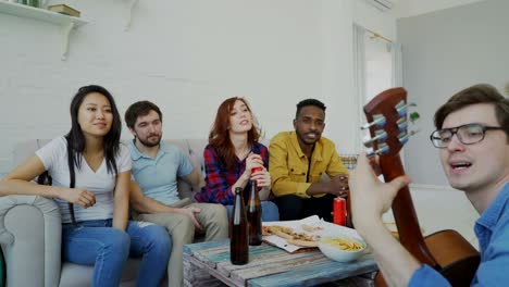 happy young friends have party playing guitar and singing together at home