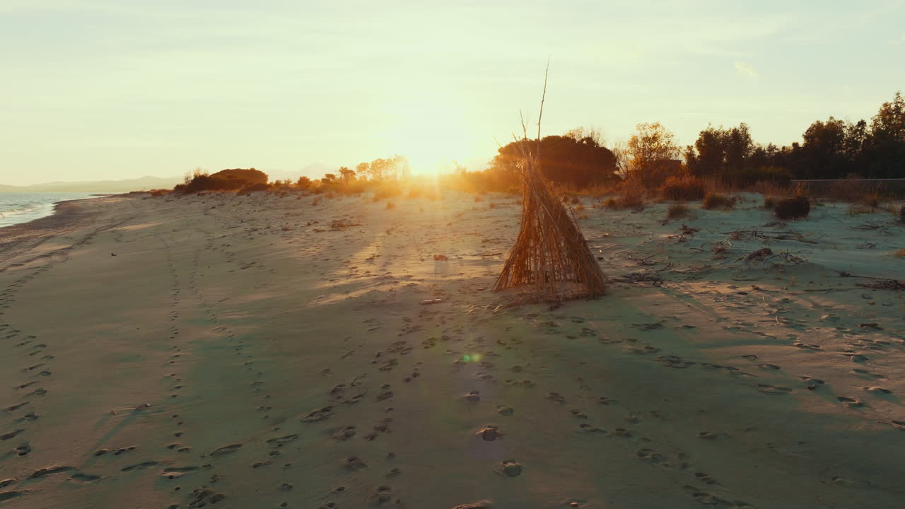 Abandoned hut on sandy beach near ocean at sunny sunset