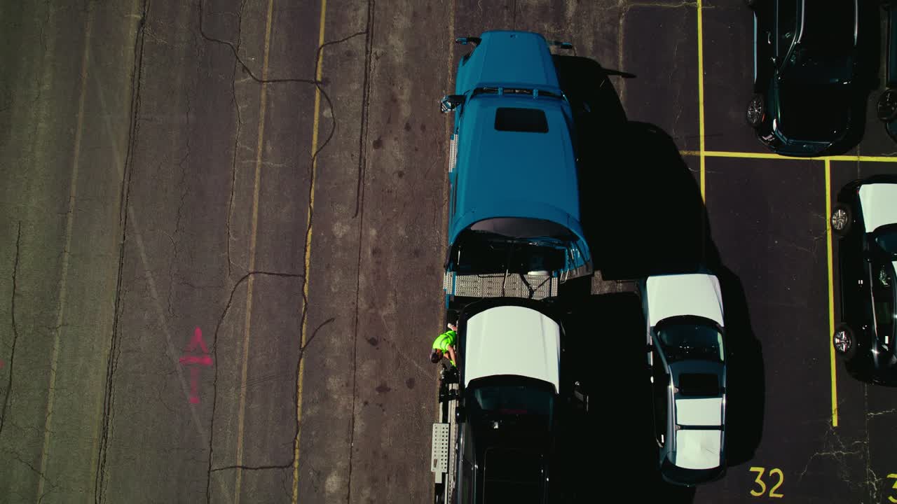A worker ties a vehicle down to the car hauler truck for transport. Top view.
