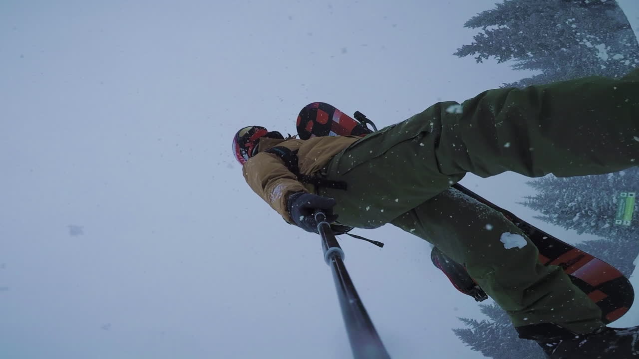 un snowboarder camina en medio de una tormenta de nieve, llevando su tabla de snowboard a un lado