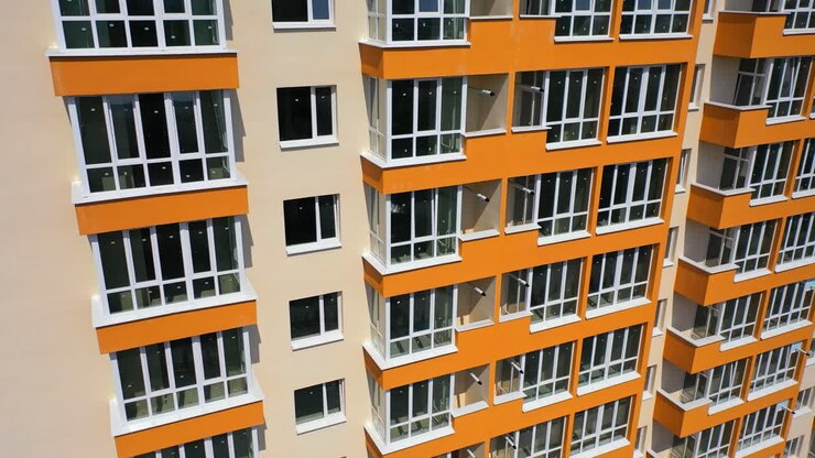 Building exterior of city multi-story apartment building. Facade of skyscraper building with new plastic windows and orange balconies at sunshine.