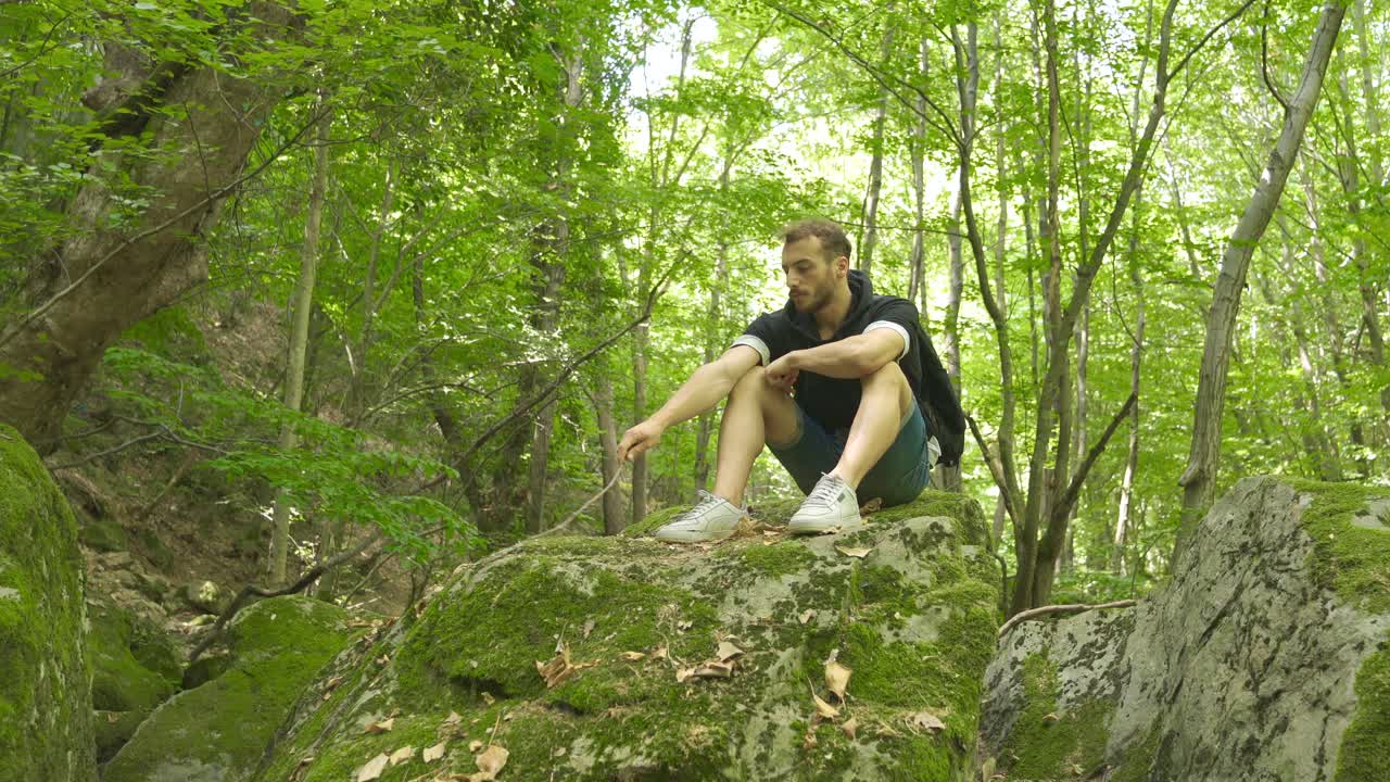 숲 속의 사려 깊은 젊은이가 바위 위에 앉아 있습니다.