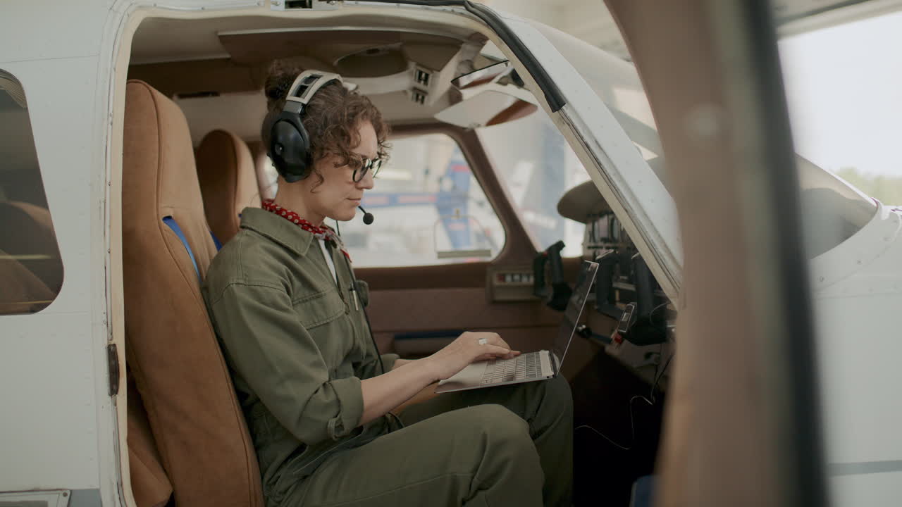 Female Pilot Checking Aircraft Systems with Laptop and Talking on Headset