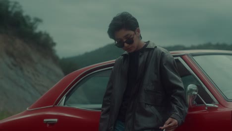 man in leather jacket beside a classic red car