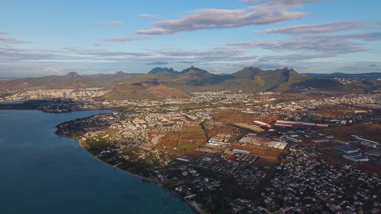 Aerial view of Mauritius at sunset, revealing the island’s coastline, cityscape, and volcanic mountains bathed in golden light. Concept of tropical paradise, exploration, and island beauty