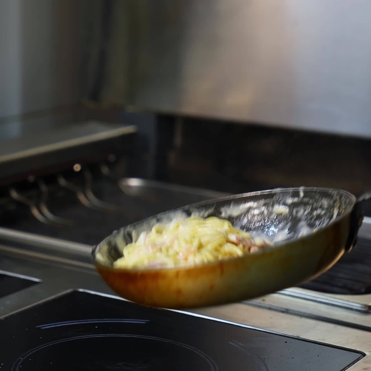 Spaghetti with bacon, herb and egg on frying pan. Chef turns carbonara on frying pan. Tasty dishes