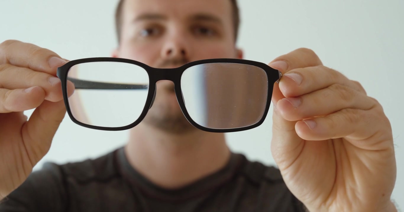 Hombre sosteniendo gafas con lentes sucios y empañados frente a la cámara. Adecuado para problemas de visión, conceptos de limpieza, cuidado óptico, mantenimiento, higiene y temas de gafas.