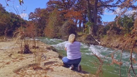 Woman-walking-by-fast-flowing-river-in-autumn-full-of-autumn-colors-taking-photos