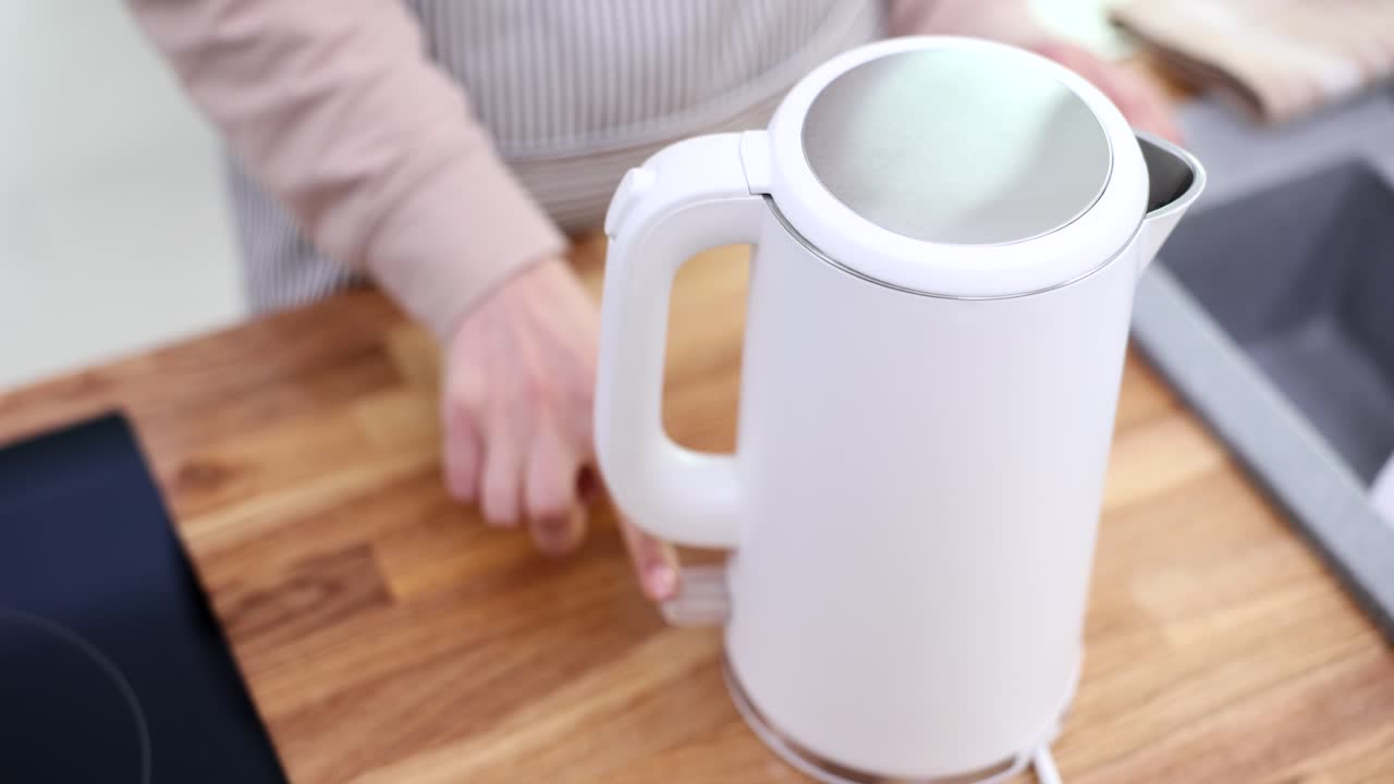 A person holding a white electric kettle in a kitchen