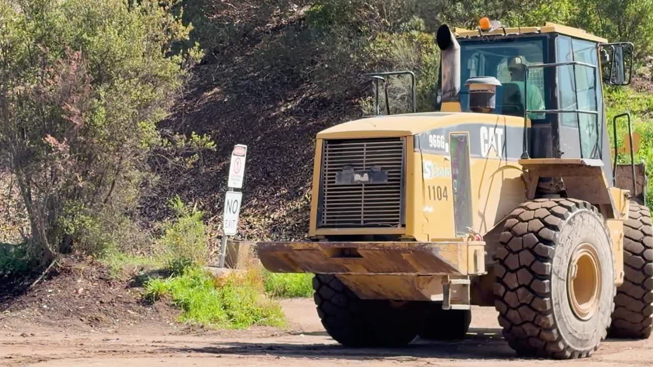 En tung hjullæsser transporterer og dumper gamle dæk på en solrig industriel genbrugsplads