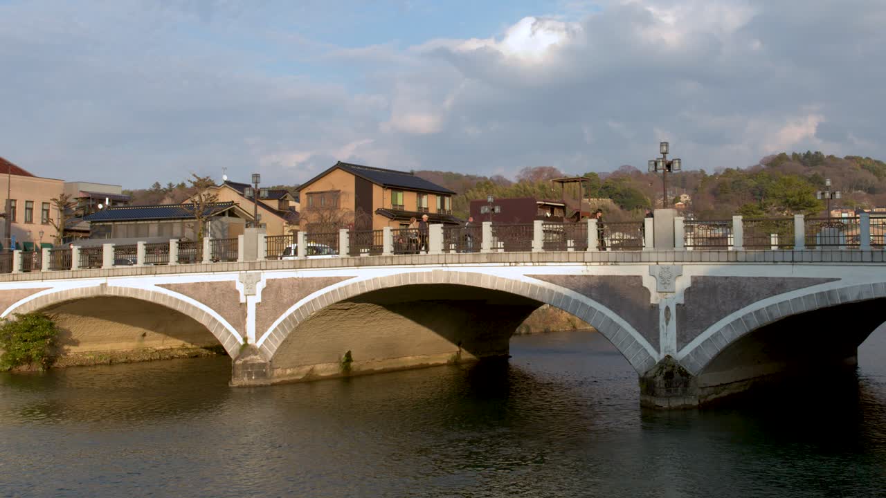 Ripresa grandangolare statica di un ponte in pietra a più archi che attraversa un fiume sotto un cielo nuvoloso.
