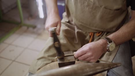 instrument maker hammering metal bar into shape on anvil to forge a flute key for a transverse flute