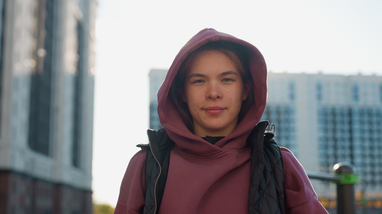 Portrait of female trainer taking break with relief on her facial expression under bright sun in urban park workout setting wearing hoodie and vest showing calm confidence and focus