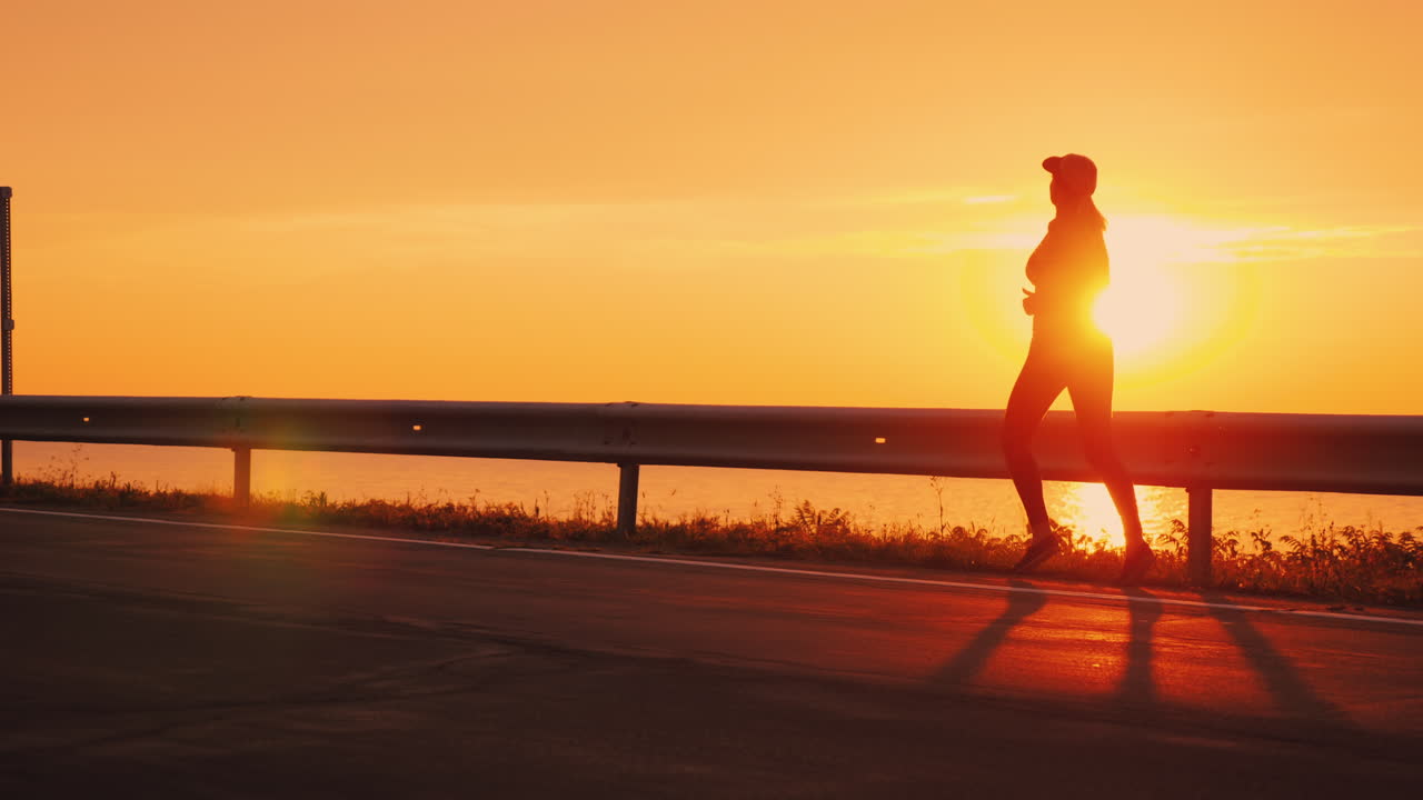 mujer atlética delgada corriendo por la carretera contra el cielo naranja y el sol poniente