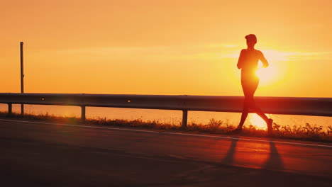 slim athletic woman running along the road against the orange sky and the setting sun