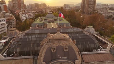 evocative 4k slow-motion footage of the chilean flag gently waving atop de chile's fine art museum as the sun sets, creating a picturesque scene. 30fps.