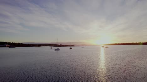 Sun-rising-over-a-calm-ocean-with-moored-sailboats-aerial