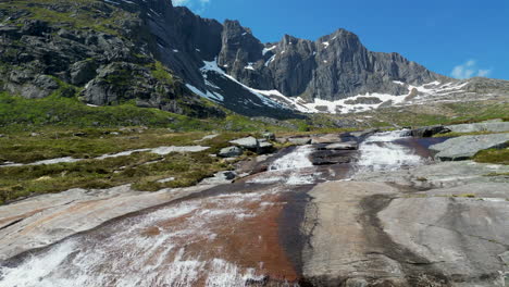 Aerial-view-in-orbit-over-the-beautiful-Molneva-waterfall-and-fantastic-snow-capped-mountains-in-the-background