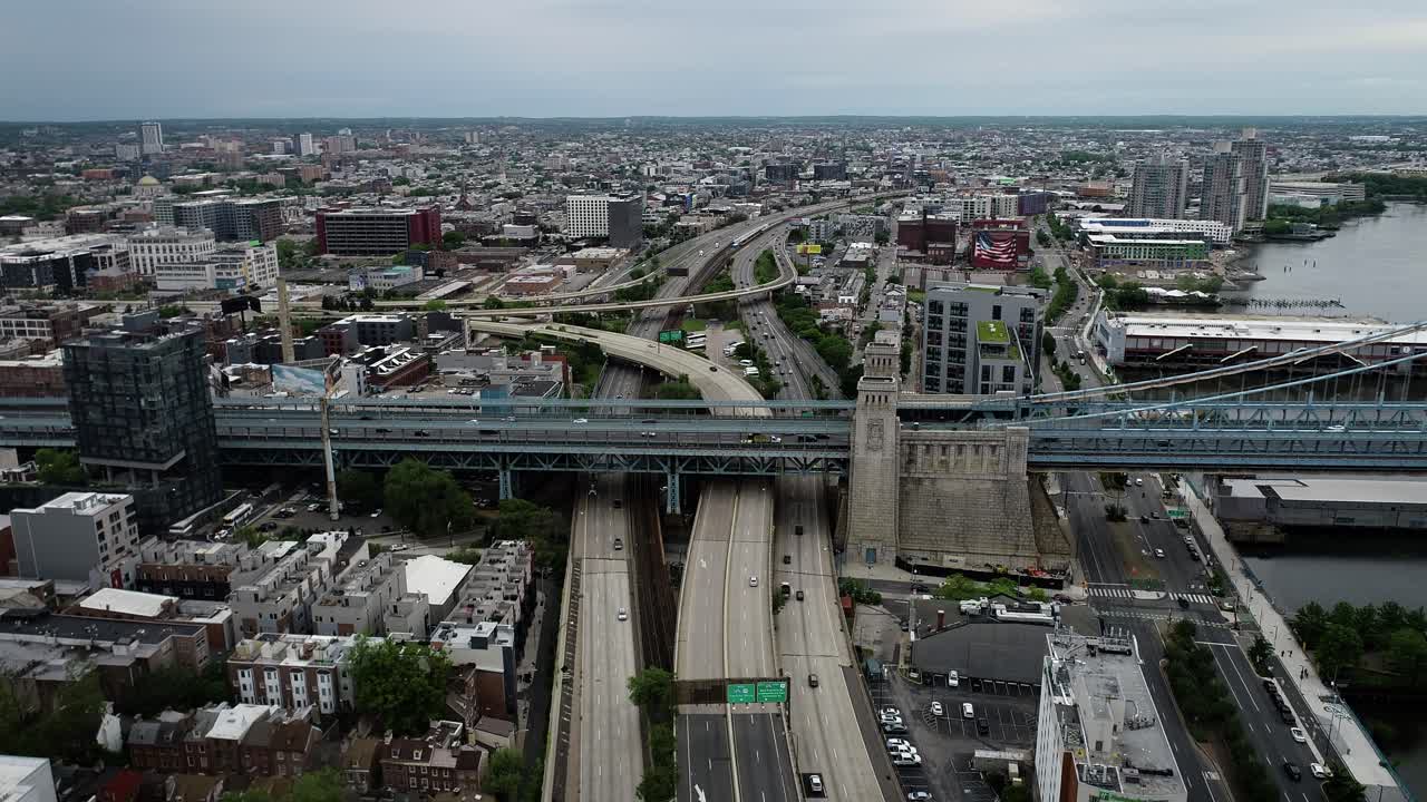 Aerial video of a highway and bridge interchange in Philadelphia, Pennsylvania. The Benjamin Franklin Bridge is in view and the camera faces the Northeast Region of Philly.