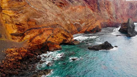 Drone-view-captures-the-stunning-red-colored-cliffs-surrounding-Sao-Lourenco-on-Madeira-Island,-creating-a-breathtaking-contrast-against-the-azure-sea