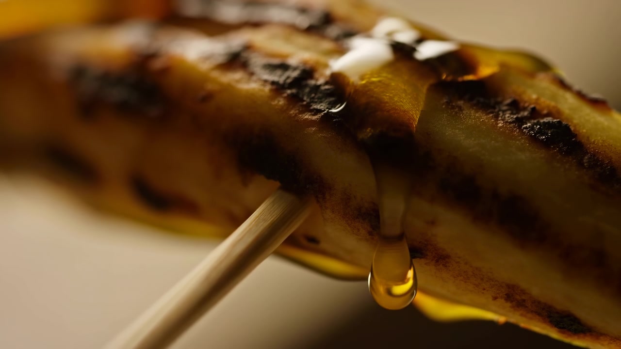 Banana grigliata su spiedino che caramella a metà sequenza sotto una calda luce da cucina.