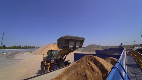 Outdoor plant for making new asphalt. Excavator pouring mixed asphalt. Manufacturing background at daytime.