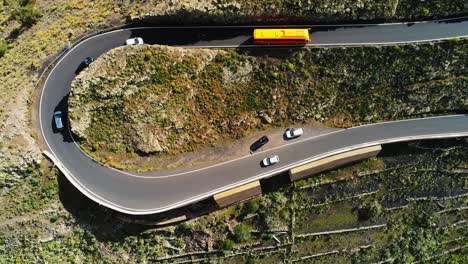 Winding-mountain-road-of-Lanzarote-with-bus-and-vehicles-driving,-aerial-top-down-view