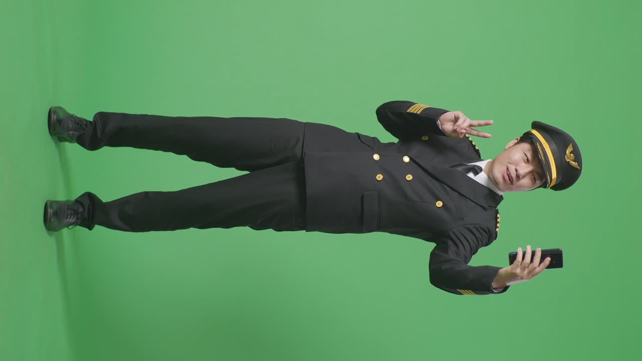 녹색 스크린 배경 스튜디오에 서서 사진을 찍는 스마트폰을 사용하는 아시아 남성 조종사