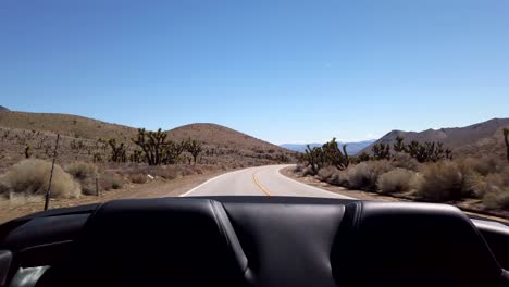 rear view out of a moving convertible car as the desert road of walker pass curves away between the mountains in the far distance