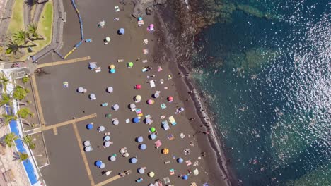 busy beach in tenerife, full of tourists sunbathing and swimming