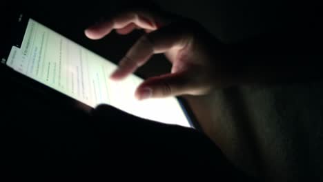 young man holding tablet touch screen the device in his hands and he is scrolling the screen while searching for pictures or reading news feed online at night room