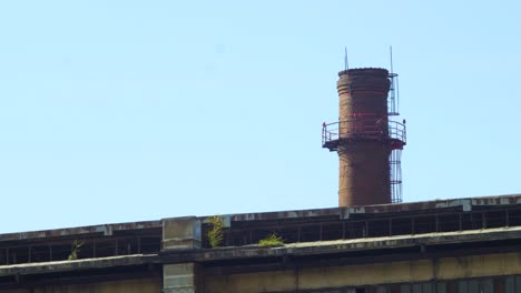 Exterior-view-of-abandoned-Soviet-heavy-metallurgy-melting-factory-Liepajas-Metalurgs-territory,-distant-red-brick-chimney,-sunny-day,-medium-shot