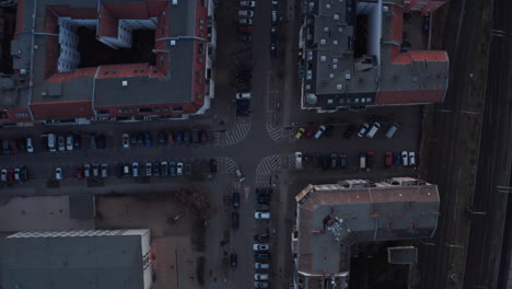 Top-down-slow-motion-view-of-empty-rooftop-and-terrace-of-residential-houses-with-vehicles-parked-and-moving-across-lane-during-early-dark-morning-in-Berlin,-Germany