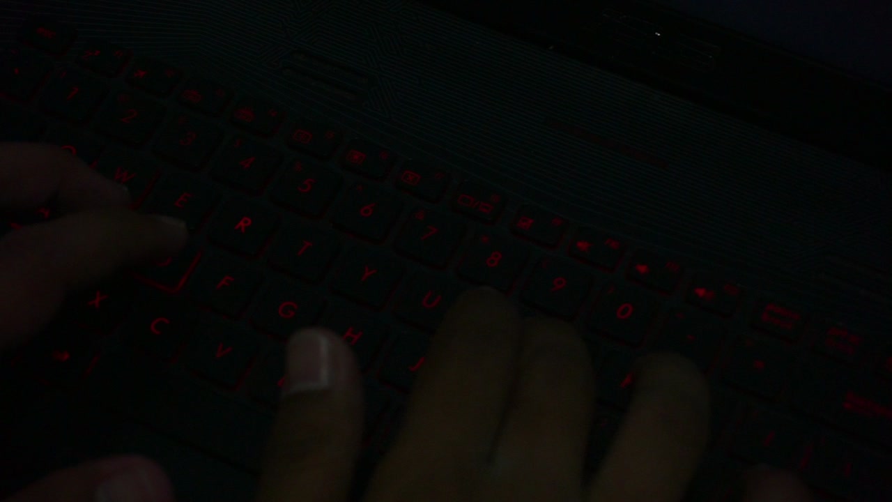 Top view of hand typing on red lighting keyboard of laptop in dark room,close up shot