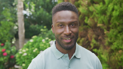 retrato de un hombre afroamericano sonriente mirando a la cámara en el jardín